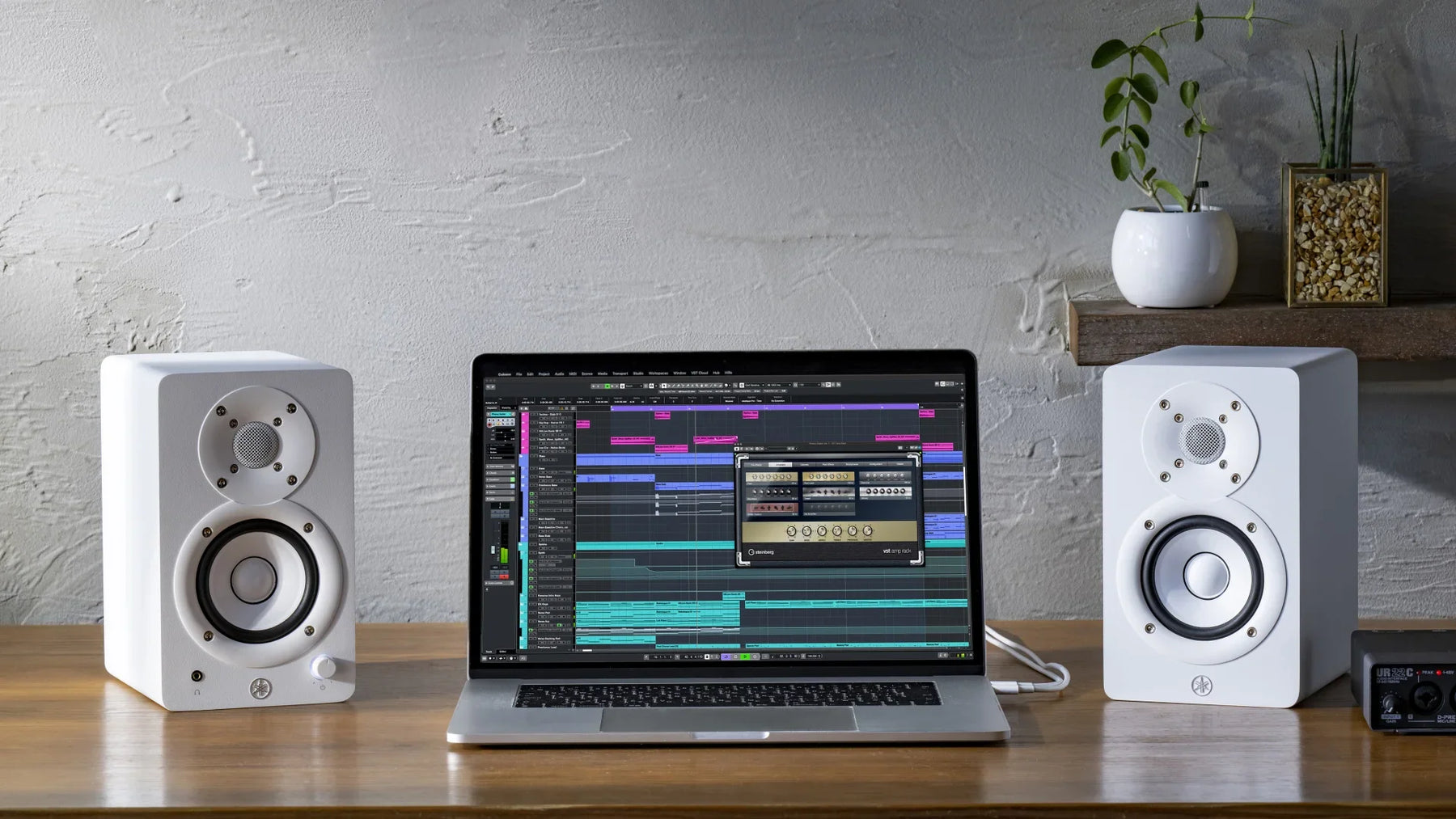 To hvite Yamaha HS3W studiomonitorer på et trebord med en bærbar PC mellom